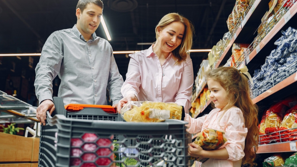 Um homem, uma mulher e uma criamçano supermercado, a criança segura produtos e os pais olha para ela